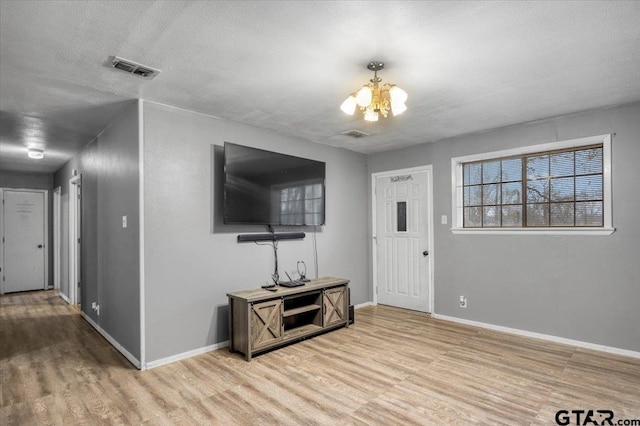 foyer featuring baseboards, visible vents, light wood-style flooring, a textured ceiling, and a notable chandelier