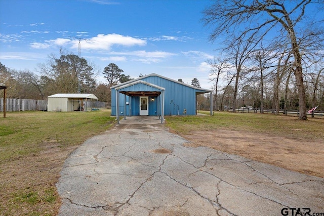 view of pole building featuring driveway, fence, and a lawn