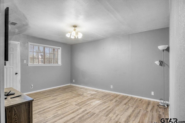 unfurnished bedroom featuring light wood finished floors, visible vents, baseboards, and an inviting chandelier