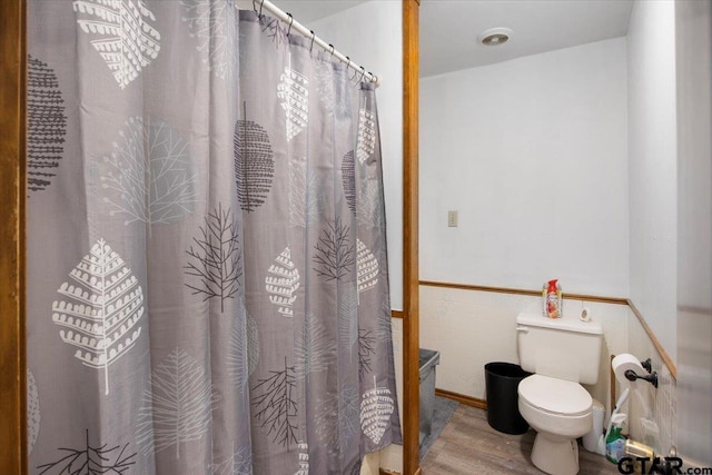 bathroom featuring toilet, a wainscoted wall, tile walls, and wood finished floors