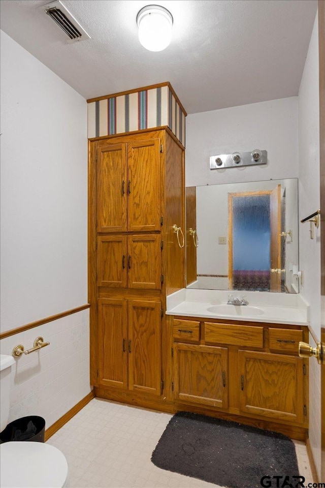 bathroom with toilet, vanity, visible vents, wainscoting, and tile patterned floors