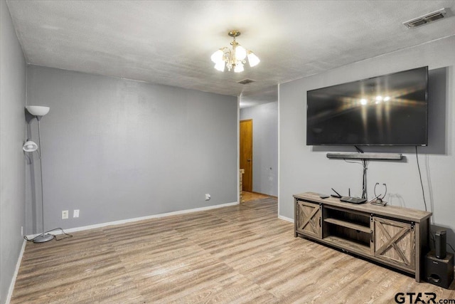 living room with baseboards, light wood finished floors, visible vents, and an inviting chandelier