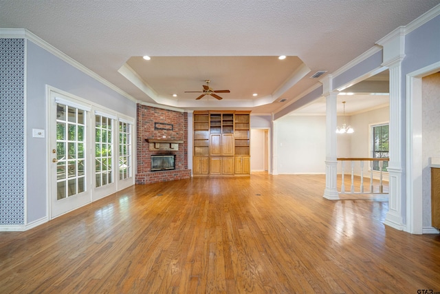 9211 Elm Tree Cir, Tyler, TX 75703 - unfurnished living room featuring a brick fireplace, a raised ceiling, wood finished floors, a ceiling fan, and a chandelier