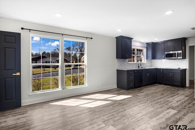 kitchen with light wood-style flooring, a sink, baseboards, decorative backsplash, and stainless steel microwave