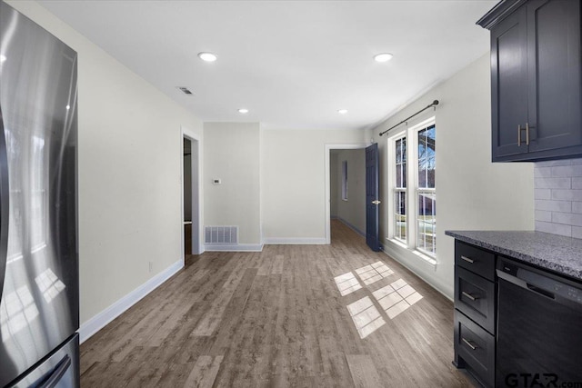 kitchen with wood finished floors, visible vents, black dishwasher, freestanding refrigerator, and decorative backsplash