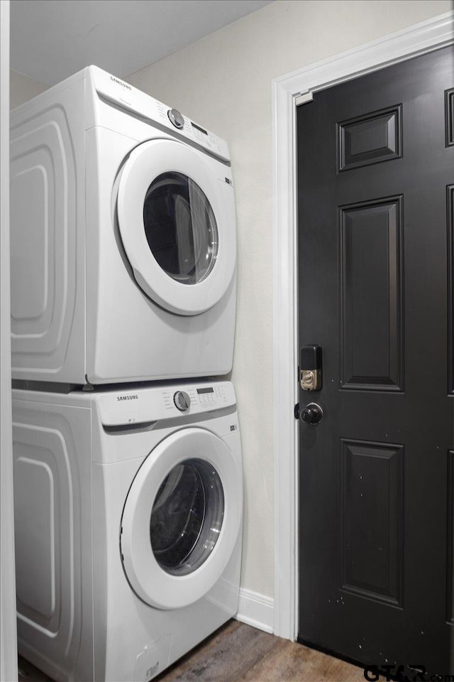 washroom featuring stacked washing maching and dryer, baseboards, laundry area, and wood finished floors