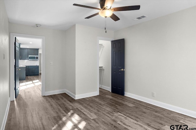 empty room with ceiling fan, wood finished floors, visible vents, and baseboards