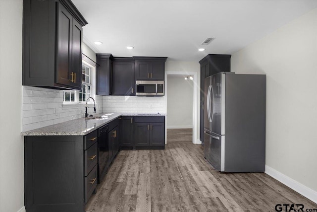 kitchen featuring baseboards, decorative backsplash, light wood-style flooring, appliances with stainless steel finishes, and a sink