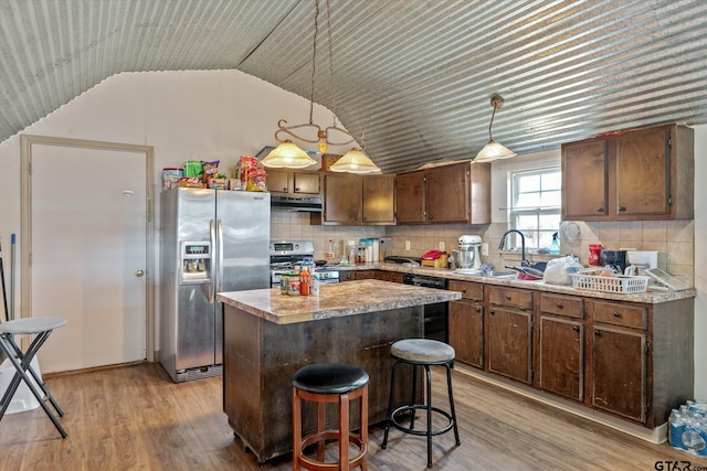 kitchen featuring light wood finished floors, under cabinet range hood, decorative backsplash, stainless steel appliances, and a sink