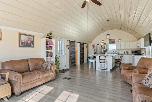 living room with visible vents, a ceiling fan, wood finished floors, a barn door, and vaulted ceiling