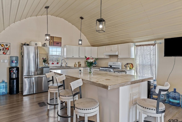 kitchen with white gas stove, a sink, under cabinet range hood, dark wood finished floors, and freestanding refrigerator