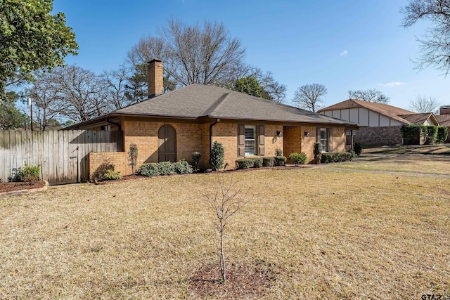 view of front of house with brick siding, fence, roof with shingles, a front yard, and a chimney