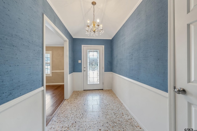 foyer featuring a wainscoted wall, wallpapered walls, ornamental molding, vaulted ceiling, and a chandelier