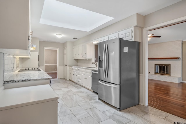 kitchen with a ceiling fan, a sink, appliances with stainless steel finishes, white cabinets, and decorative backsplash