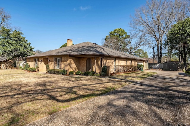 view of property exterior featuring a lawn, a chimney, driveway, and fence