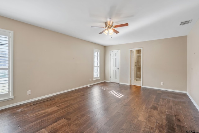 empty room with dark wood-type flooring, a ceiling fan, visible vents, and baseboards