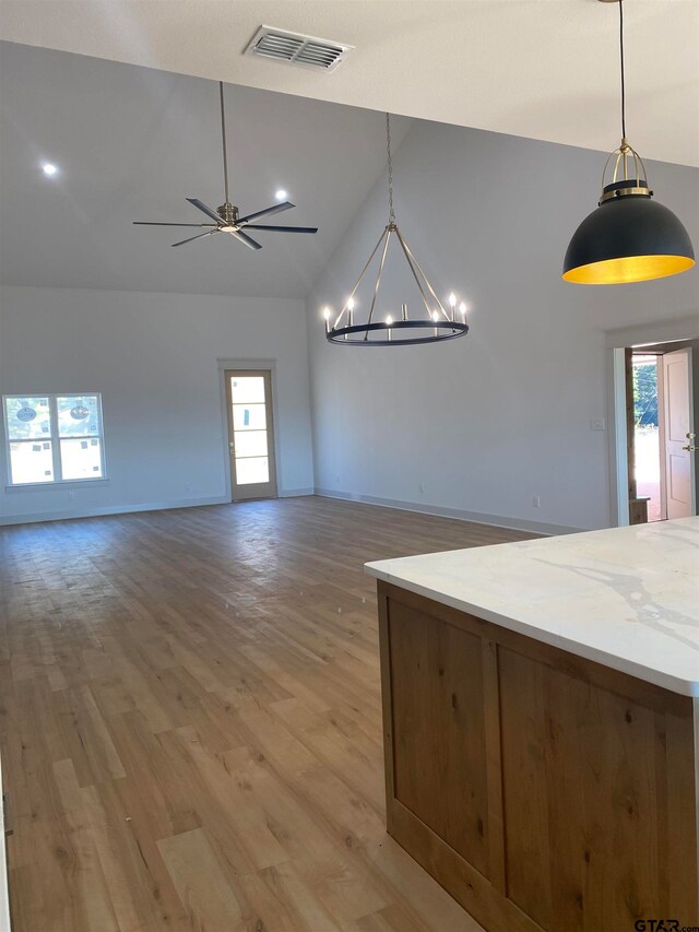 interior space with ceiling fan with notable chandelier, lofted ceiling, light stone counters, hardwood / wood-style floors, and hanging light fixtures