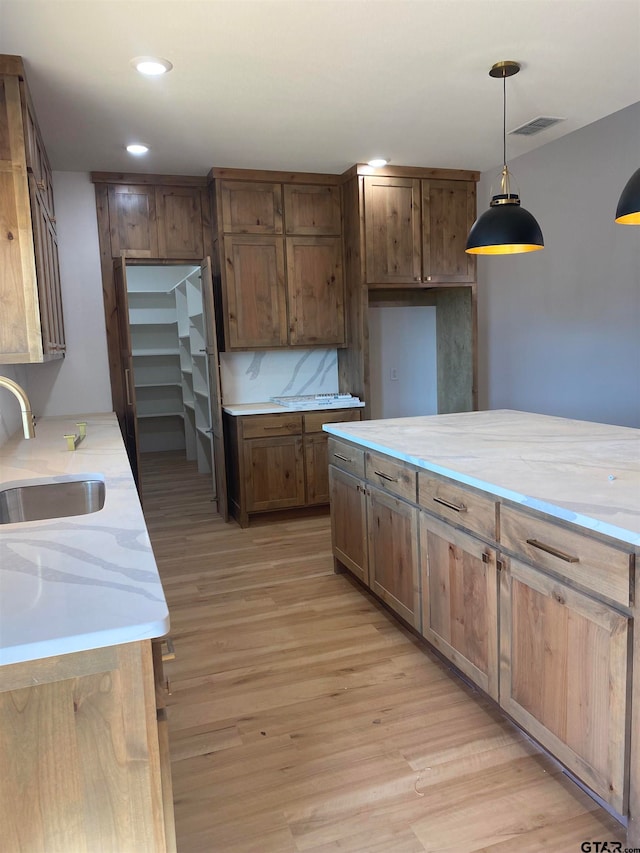 kitchen with light hardwood / wood-style floors, sink, light stone counters, decorative light fixtures, and decorative backsplash