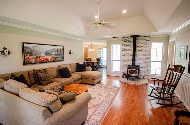 living room featuring hardwood / wood-style flooring, ceiling fan, a raised ceiling, a wood stove, and crown molding