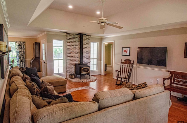 living room with ceiling fan, hardwood / wood-style floors, a raised ceiling, a wood stove, and crown molding