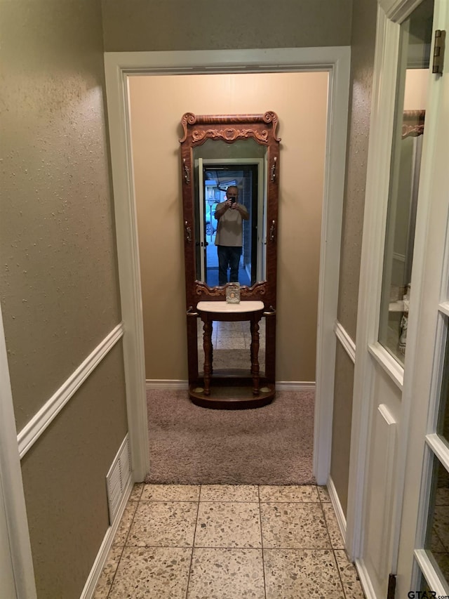 hall featuring baseboards, light carpet, and visible vents