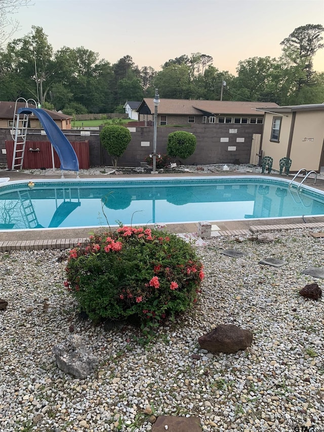pool at dusk with a water slide, a fenced backyard, and an outdoor pool