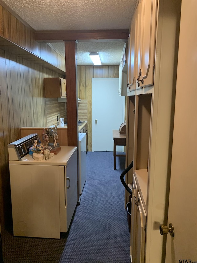 washroom with a textured ceiling, cabinet space, dark colored carpet, wooden walls, and washer and dryer