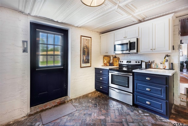 kitchen featuring white cabinets, appliances with stainless steel finishes, brick floor, light countertops, and blue cabinetry