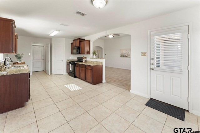 kitchen with light tile patterned flooring, light stone countertops, sink, and black appliances