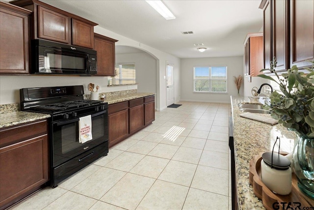 kitchen with light stone countertops, sink, light tile patterned floors, and black appliances