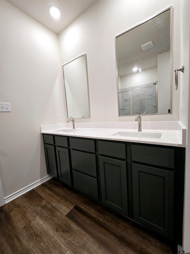 full bathroom with wood finished floors, a stall shower, double vanity, and baseboards