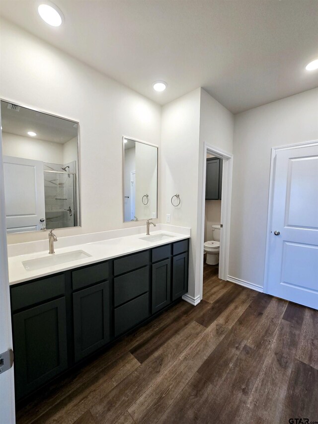 bathroom with a stall shower, wood finished floors, toilet, double vanity, and recessed lighting