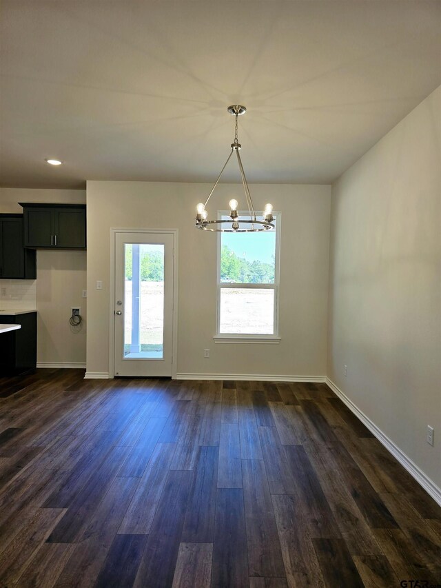 unfurnished dining area featuring a chandelier, dark wood-style floors, and baseboards