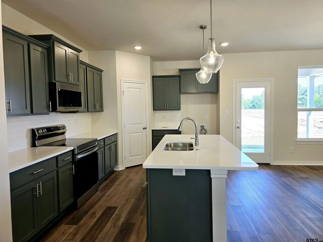 kitchen featuring stainless steel appliances, a sink, dark wood-type flooring, tasteful backsplash, and a center island with sink