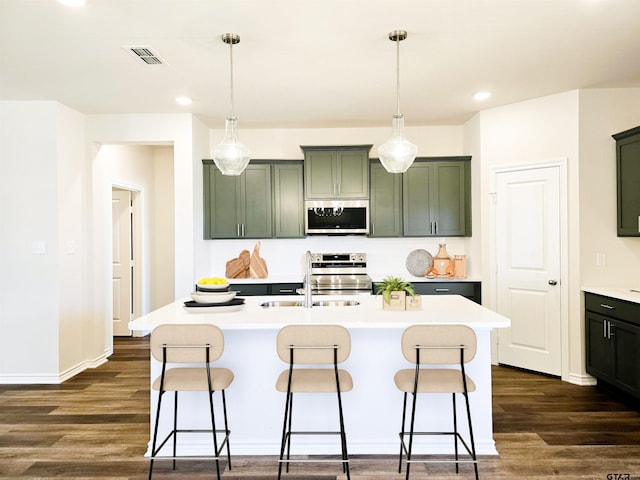 kitchen with appliances with stainless steel finishes, green cabinetry, a sink, dark wood-style flooring, and recessed lighting
