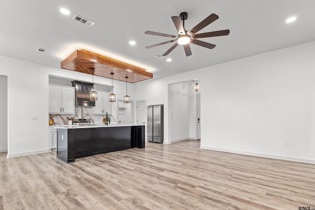 kitchen with decorative backsplash, light wood-type flooring, ceiling fan, hanging light fixtures, and an island with sink