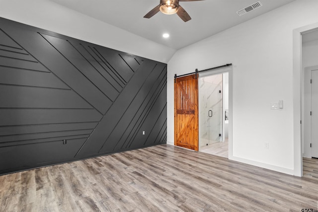 empty room with ceiling fan, a barn door, and light hardwood / wood-style floors