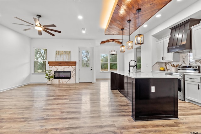 kitchen featuring plenty of natural light, stainless steel range with electric cooktop, hanging light fixtures, and an island with sink