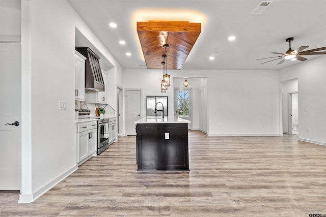 kitchen with hanging light fixtures, appliances with stainless steel finishes, white cabinetry, and a kitchen island with sink