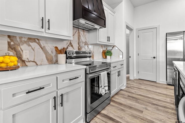 kitchen featuring white cabinets, light hardwood / wood-style flooring, wall chimney exhaust hood, tasteful backsplash, and stainless steel appliances