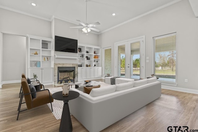 living room featuring ceiling fan, french doors, a high end fireplace, light hardwood / wood-style floors, and ornamental molding