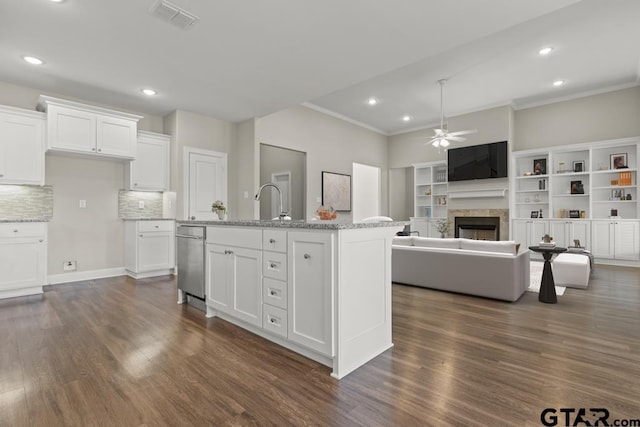 kitchen with white cabinets, light stone counters, ceiling fan, and an island with sink