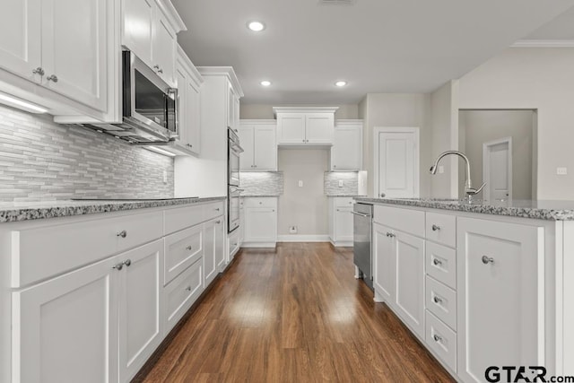 kitchen with black electric stovetop, backsplash, light stone counters, a center island with sink, and white cabinetry