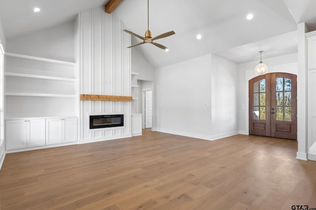 unfurnished living room featuring heating unit, french doors, a large fireplace, light wood-type flooring, and built in shelves