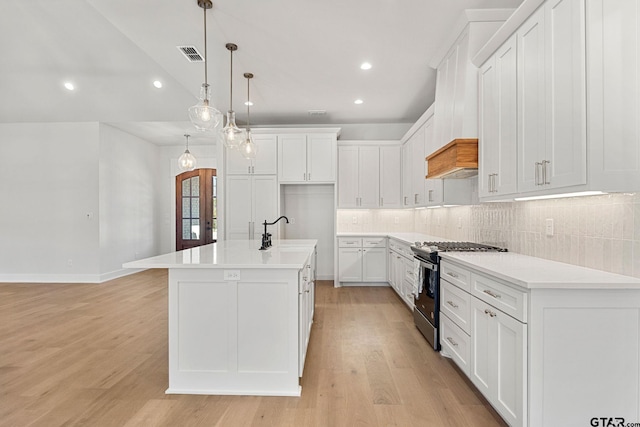 kitchen with stainless steel gas range, hanging light fixtures, a center island with sink, white cabinets, and backsplash