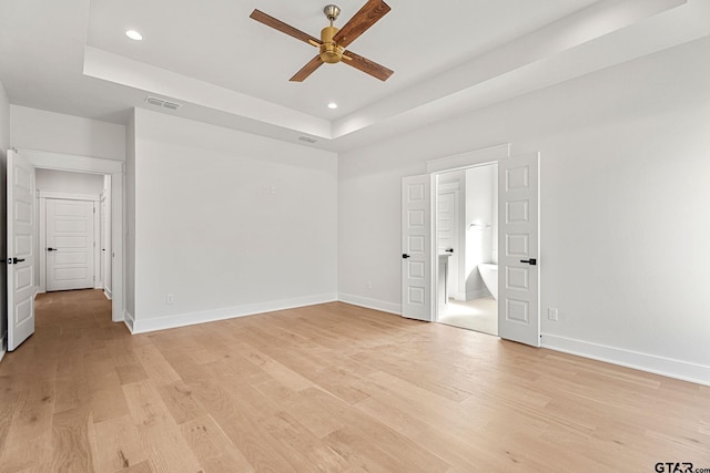 unfurnished bedroom featuring ceiling fan, connected bathroom, a raised ceiling, and light wood-type flooring