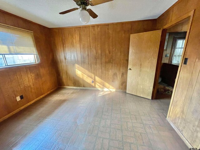 unfurnished room featuring wooden walls, a textured ceiling, and ceiling fan