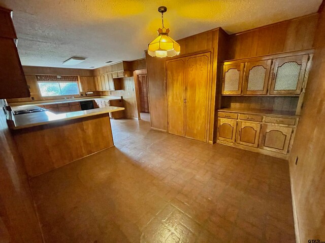 kitchen featuring wood walls, sink, kitchen peninsula, a textured ceiling, and decorative light fixtures