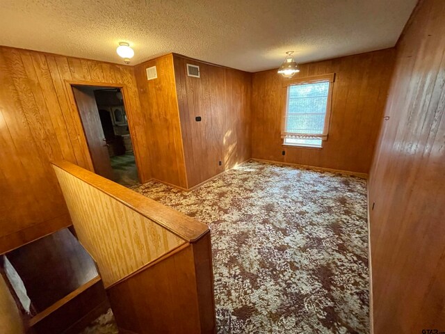 carpeted spare room featuring wood walls and a textured ceiling