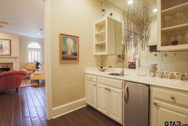 kitchen with refrigerator, sink, a brick fireplace, ornamental molding, and white cabinetry